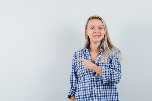 Señora rubia en camisa casual apuntando hacia el lado izquierdo y mirando feliz