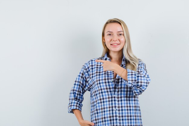 Señora rubia en camisa casual apuntando a un lado y mirando alegre