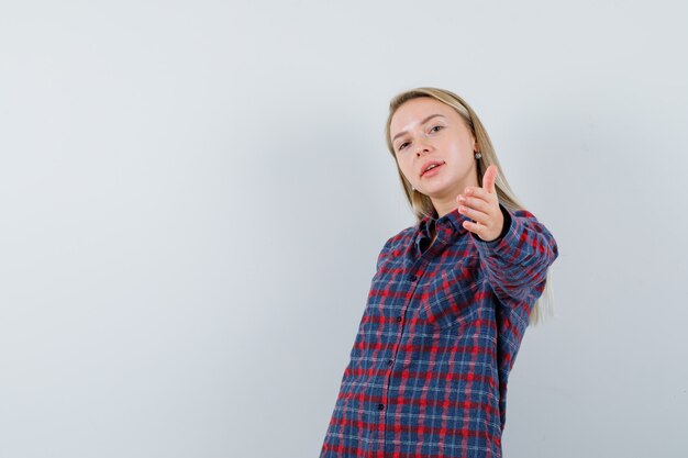 Señora rubia en camisa casual manteniendo la mano extendida y mirando alegre, vista frontal.