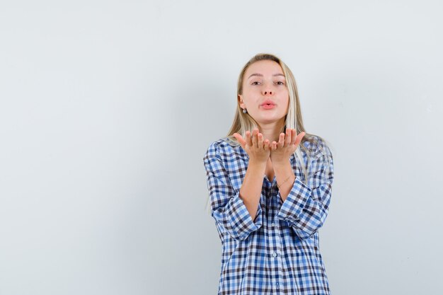 Señora rubia en camisa de cuadros soplando beso de aire con labios fruncidos