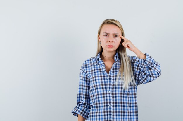 Señora rubia en camisa a cuadros sosteniendo el dedo en las sienes y luciendo estricta