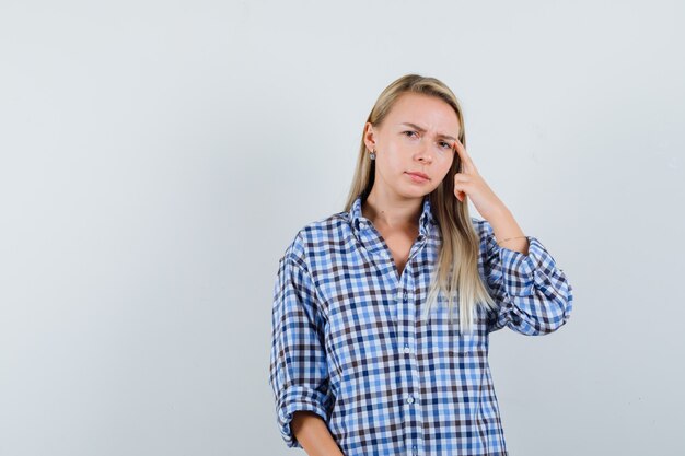 Señora rubia en camisa a cuadros sosteniendo el dedo en las sienes y mirando pensativo