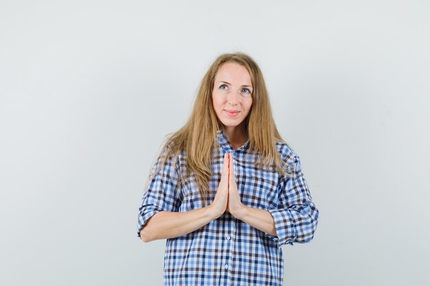 Señora rubia en camisa mostrando gesto de namaste y mirando esperanzado,