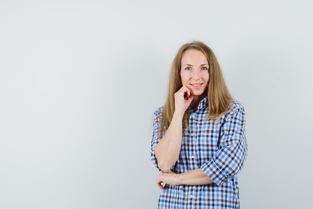 Señora rubia en camisa de pie en pose de pensamiento y mirando alegre,