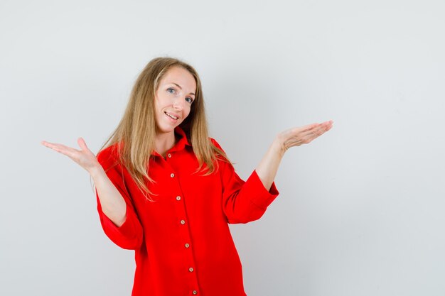 Señora rubia en camisa roja presentando o comparando algo y mirando contento,