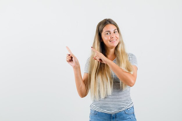 Señora rubia en camiseta apuntando a un lado y mirando alegre, vista frontal.