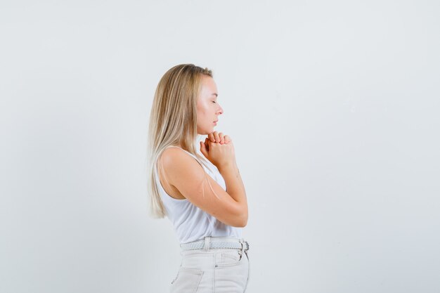 Señora rubia en camiseta, pantalones cogidos de la mano en gesto de oración y luciendo esperanzada.