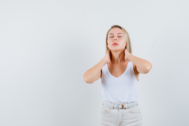 Foto gratuita señora rubia en camiseta, pantalones que sufren de dolor de cuello y lucen fatigados, vista frontal.