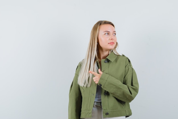 Señora rubia con chaqueta, pantalones apuntando a un lado y mirando enfocado, vista frontal.