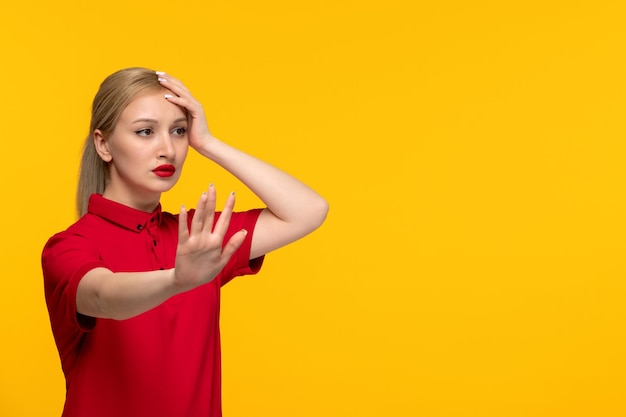 Señora rubia del día de la camisa roja que muestra la señal de stop en una camisa roja sobre un fondo amarillo
