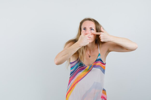 Señora rubia exprimiendo su grano en la mejilla en vestido de verano