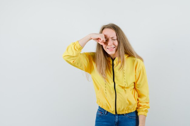 Señora rubia frotándose los ojos mientras llora en chaqueta, jeans y parece ofendida,