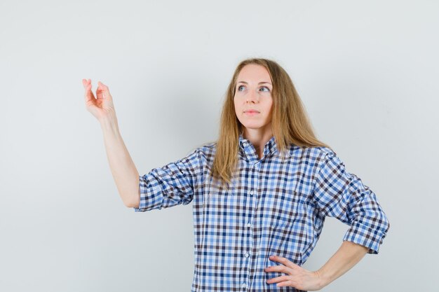 Señora rubia levantando el brazo mientras mira hacia arriba en camisa y parece esperanzada,