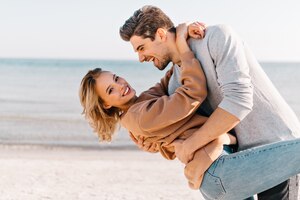 Foto gratuita señora rubia de pelo corto abrazando a marido en la playa. retrato al aire libre de hombre de buen humor bailando con su novia cerca del océano.