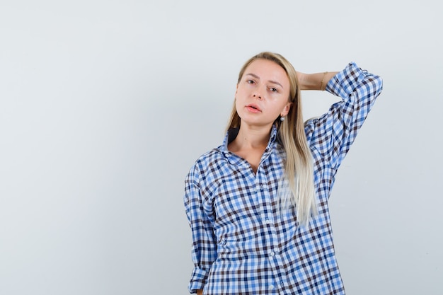 Señora rubia posando con la mano detrás de la cabeza en camisa a cuadros y luciendo agradable