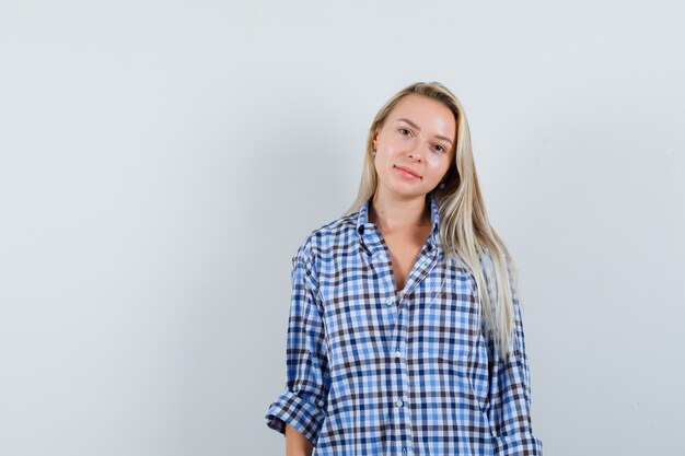 Señora rubia posando mientras está de pie en camisa a cuadros y luciendo sensato