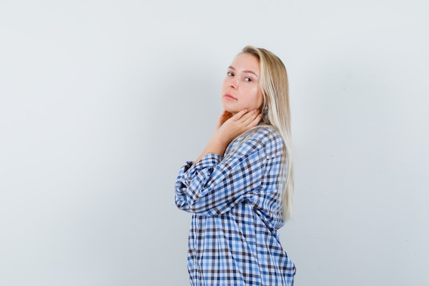 Señora rubia posando mientras está de pie en camisa a cuadros y se ve elegante. .