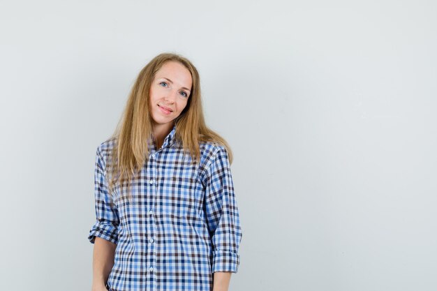 Señora rubia posando mientras está de pie en camisa y parece cautivadora.