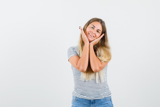 Señora rubia que cubre la cara con las manos en camiseta y parece feliz. vista frontal.