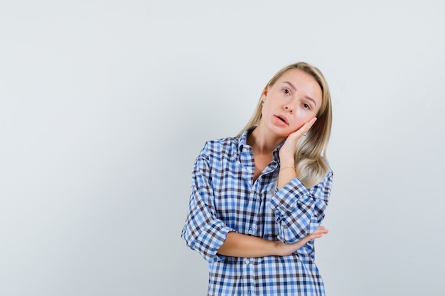 Señora rubia que se inclina la mejilla en la palma en camisa a cuadros y luciendo bonita