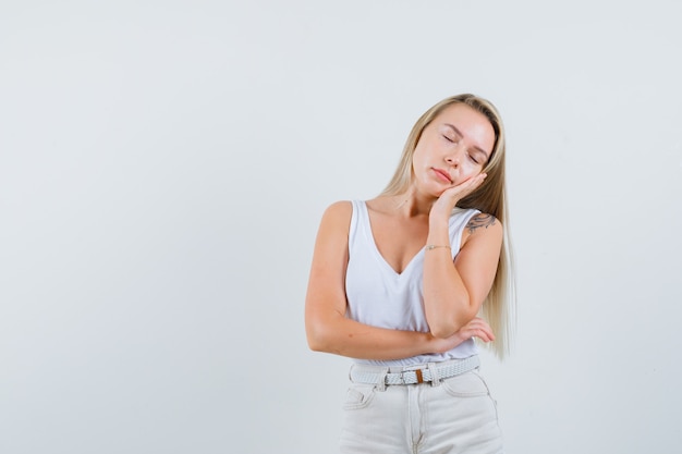 Foto gratuita señora rubia que se inclina la mejilla en la palma levantada en camiseta, pantalones y con sueño