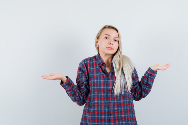 Señora rubia que muestra un gesto de impotencia en camisa casual y parece confundido. vista frontal.