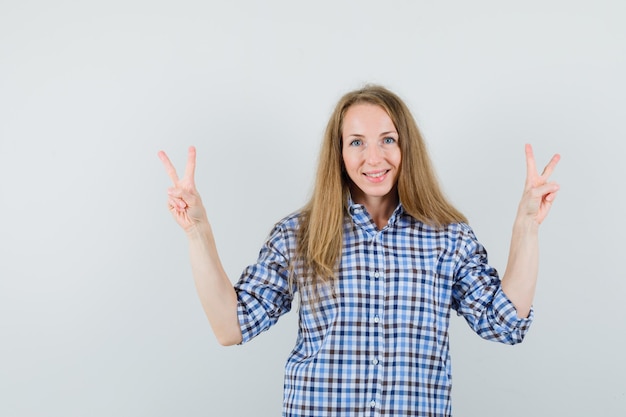 Señora rubia que muestra el signo v en camisa y parece confiada.