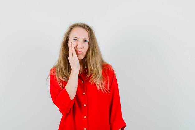 Señora rubia que tiene dolor de muelas en camisa roja y parece incómoda.