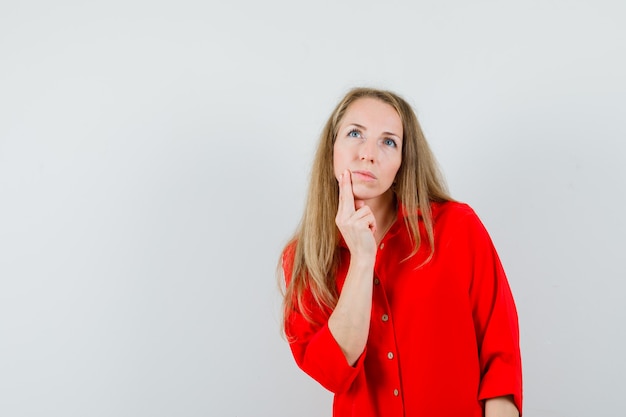 Señora rubia sosteniendo el dedo en la barbilla con camisa roja y mirando pensativo.