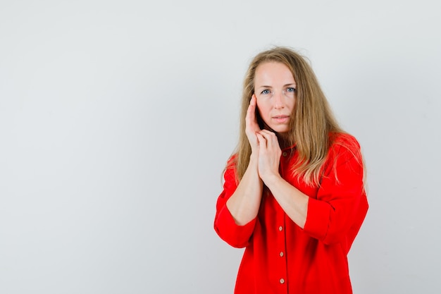 Señora rubia tocando la piel de la cara en la mejilla con camisa roja y luciendo elegante.