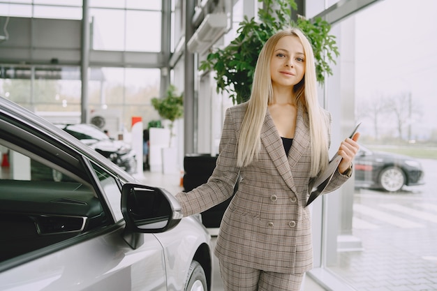 Señora en un salón de autos. Mujer comprando el coche. Mujer elegante con un traje marrón.