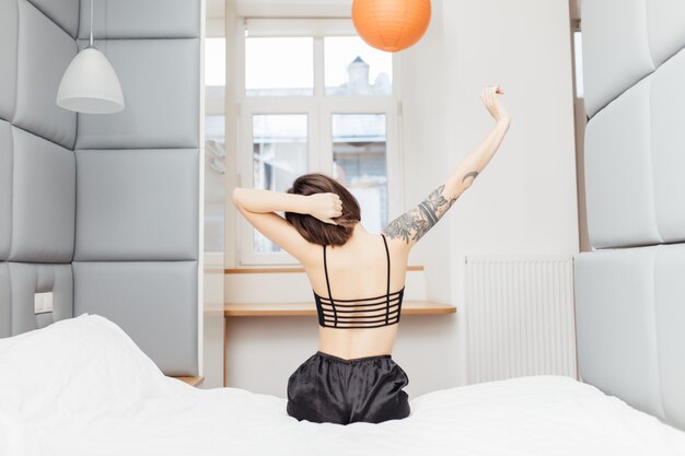 Señora sentada al borde de la cama y estirando los brazos para relajarse por la mañana después de despertarse por la mañana