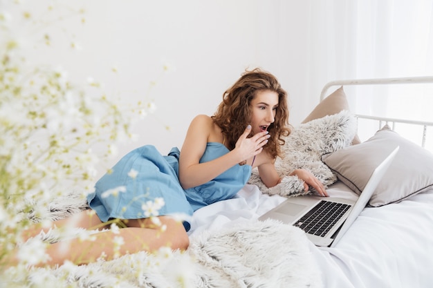 Señora sentada en el interior de la cama usando la computadora portátil. Mirando a un lado