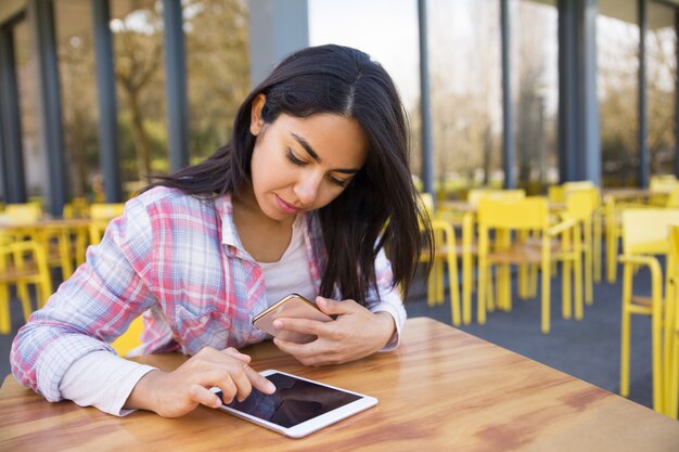 Señora seria que usa la tableta y el smartphone en café al aire libre