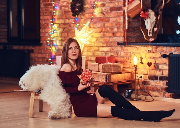 Señora sexy pelirroja posando en una habitación con interior de loft y decoración navideña.