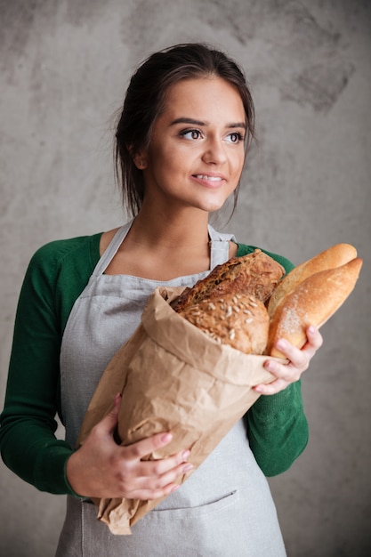 Señora sonriente panadero de pie y sosteniendo pan.