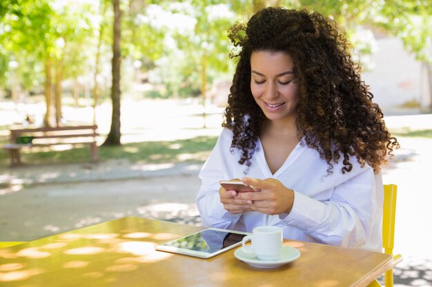 Señora sonriente con smartphone en la mesa de café en el parque