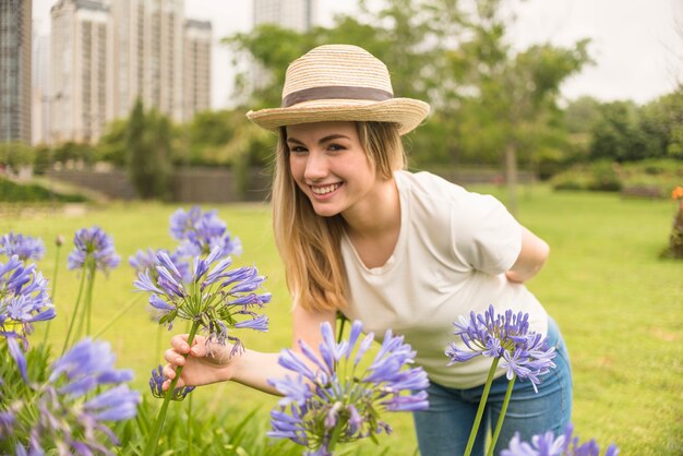 Foto gratuita señora sonriente en el sombrero que sostiene las floraciones azules en parque de la ciudad