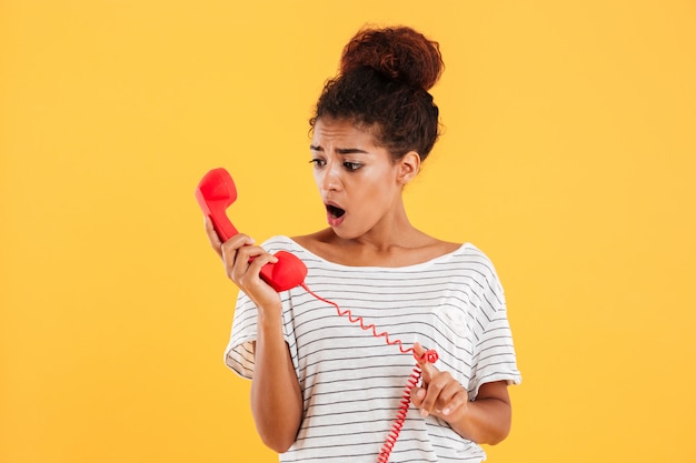 Foto gratuita señora sorprendida mirando auricular rojo aislado sobre amarillo