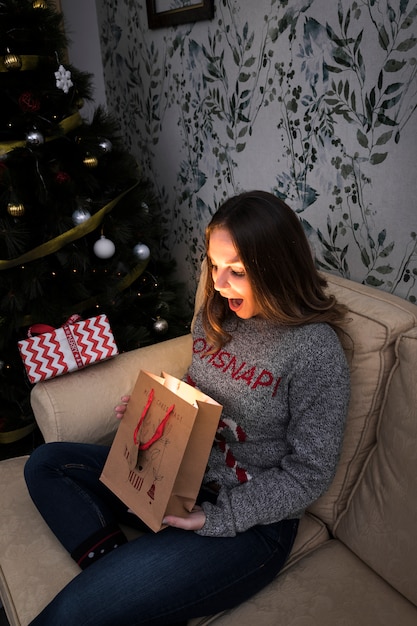 Foto gratuita señora sorprendida con el paquete de regalo en el sofá cerca del árbol de navidad