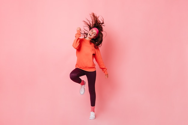 Foto gratuita señora en sudadera brillante y polainas marrones baila contra la pared rosa