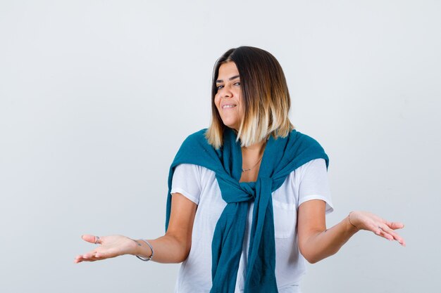 Señora con suéter atado mostrando gesto de impotencia en camiseta blanca y mirando indeciso, vista frontal.