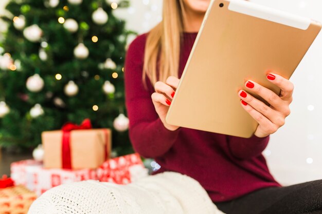 Señora con tableta cerca de cajas de regalo y árbol de navidad