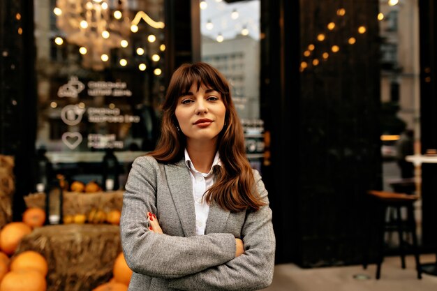 Señora en traje gris sonriendo a la cámara en el fondo del elegante café con luces.