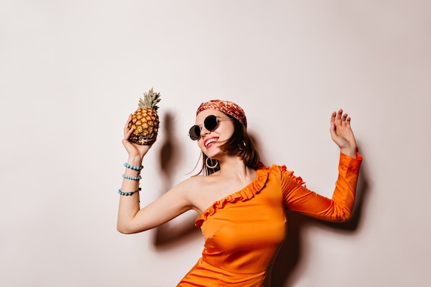 Foto gratuita señora en traje naranja se ríe, baila y sostiene la piña en el espacio en blanco.