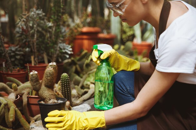 Señora en vasos de pie en invernadero cerca de las plantas.