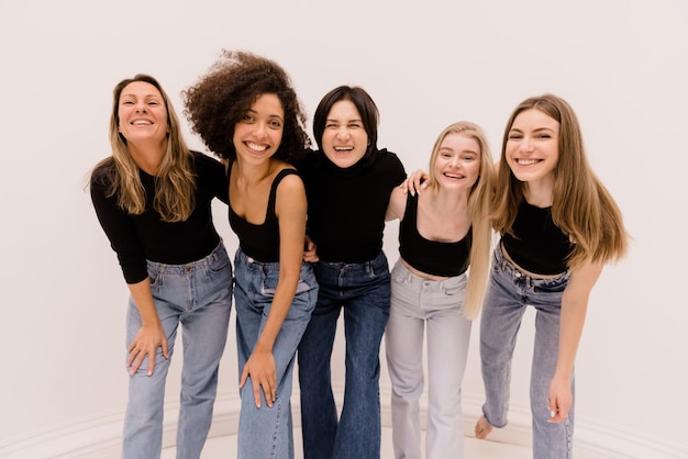 Foto gratuita señoras alegres de diferentes razas y edades en ropa básica están sonriendo inclinándose todas juntas hacia la cámara sobre fondo blanco.