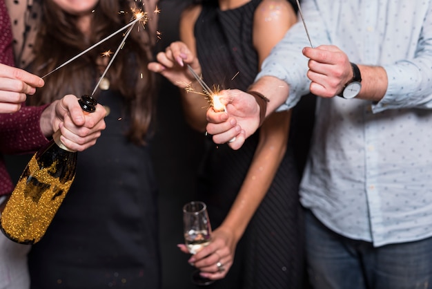 Señoras y hombres sosteniendo luces de Bengala, botella y vaso de bebida