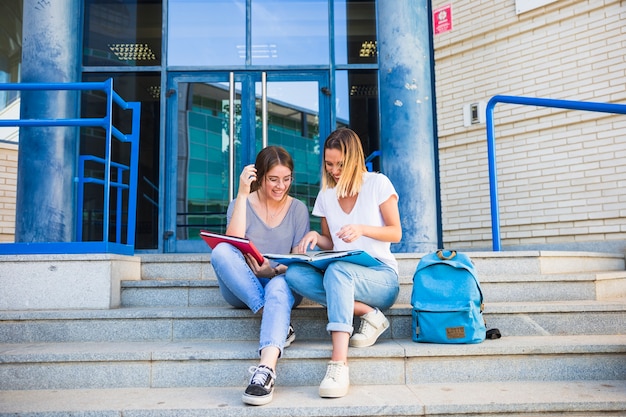 Señoras leyendo libros de texto cerca de la universidad