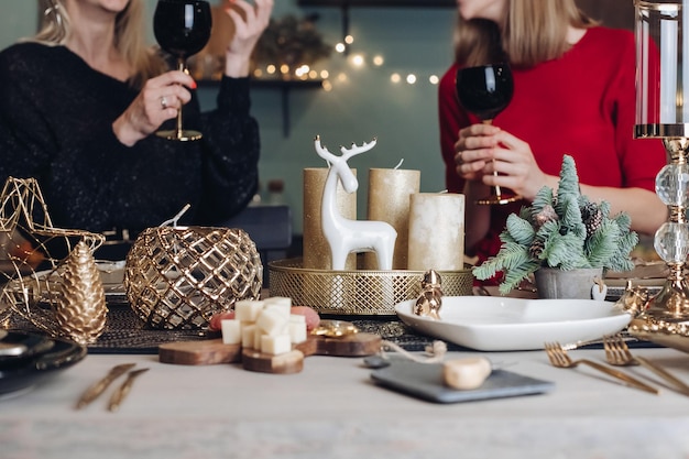 Señoras muy sonrientes brindando con copas de vino mientras celebran la Navidad en casa